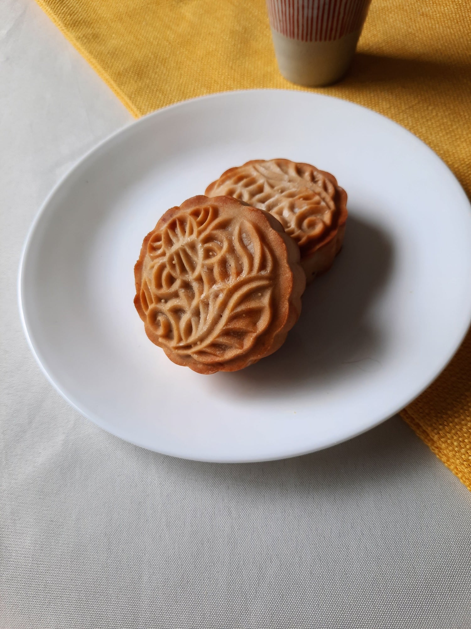 Two full, uncut red bean mooncakes stacked on a white plate.  A cup of green tea in the background.