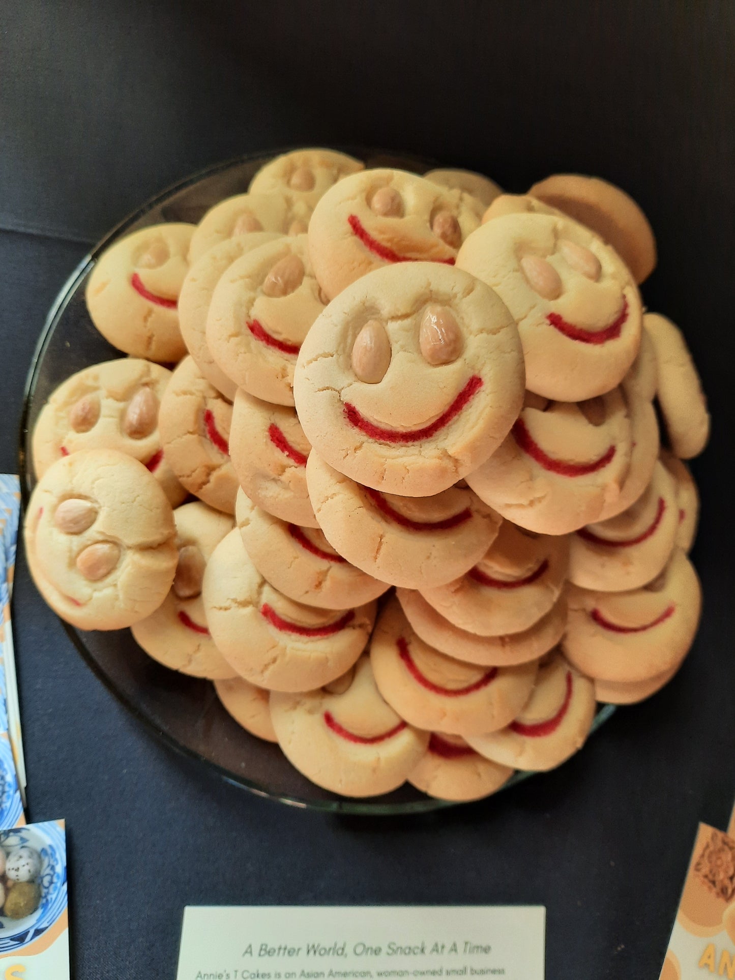 A pile of perfectly round smiley faced almond cookies on a black table. All almond cookies were made for the premier of Everything Everywhere All At Once.